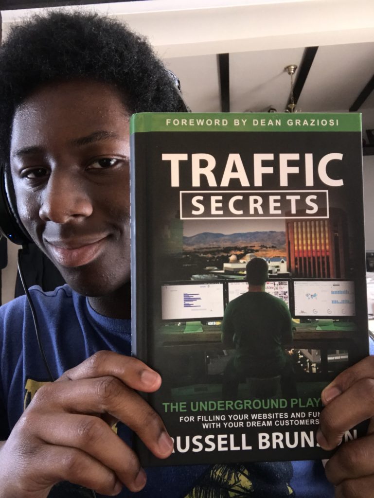 Image of Adventago in his house  holding the traffic secrets book that will help you get more sellers in your property investing career